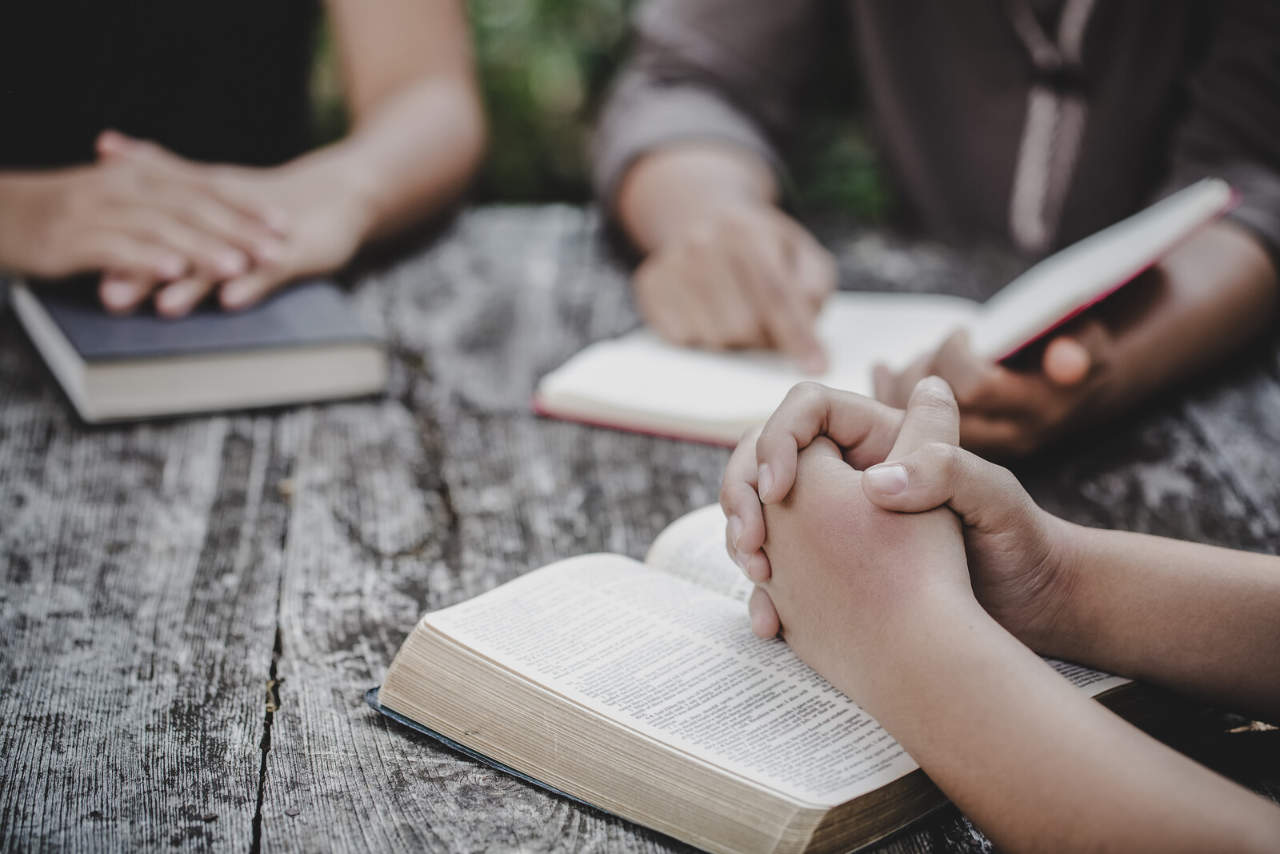 Women sat round table praying and reading bibles