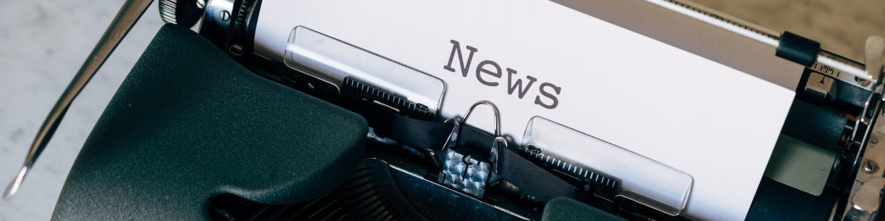 Paper with News written on coming out of typewriter